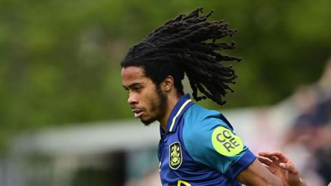 Neo Eccleston playing for Huddersfield Town in their away kit of blue with lime trim