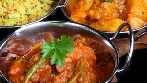 A dark orange curry in a silver Balti bowl with a sprig of coriander and green chillies on top.