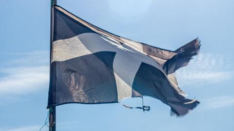 A picture of the Saint Piran's Flag the flag of Cornwall flying on a clear sunny day. The flag is black with a white cross on it. 
