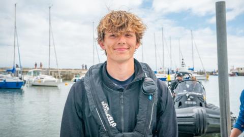 Harry Besley wearing a black life jacket, standing on the dock in Lyme Regis harbour