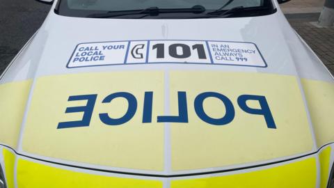 A police car with a call 101 or 999 message on its bonnet