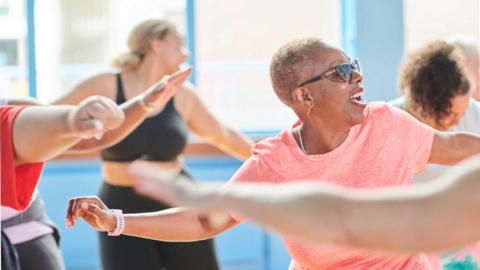 Women at the gym smiling and dancing with their arms raised.