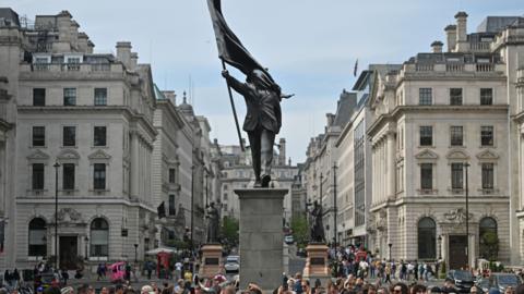 The Banksy statue is of a man holding up a flag with his right arm and the flag drapes over his face.