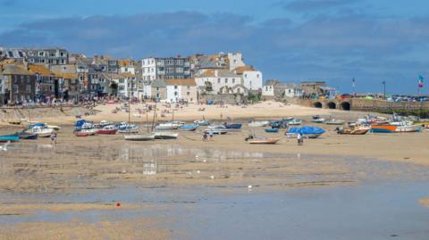 St Ives harbour on a cloudy but sunny day. Lots of boats are on the sand during low tide.