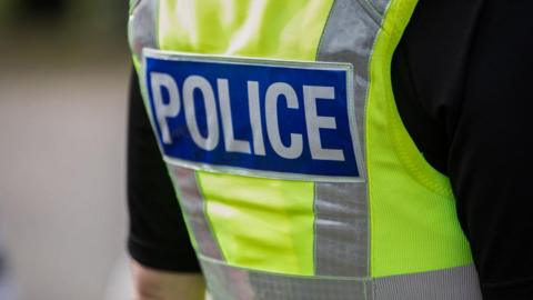 A person wearing a high vis vest with 'Police' written in white writing on a blue background. 