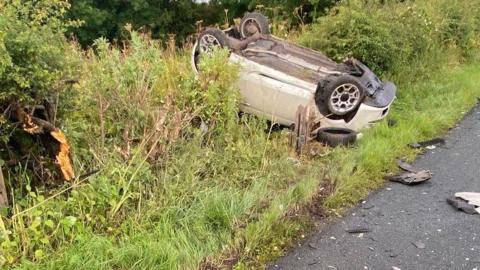 White Fiat 500 on its roof in a grass ditch