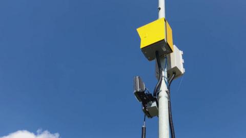 A yellow box with two sensors, attached to a lamppost.