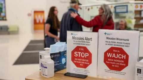 People stand near healthy awareness posters related to the measles outbreak during a public health awareness campaign, at the Taber Health Centre, in the largely Mennonite community of Taber, Alberta, Canada, October 27, 2025.