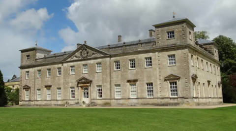 Old stately home with many windows and a neat green lawn around it.