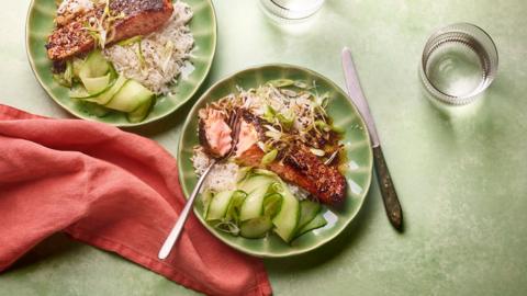 Top down view of a green plates on a green tablecloth with salmon rice and veg on the plate.