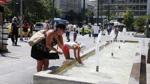 people splashing water on themselves from a water fountain on a street in Europe