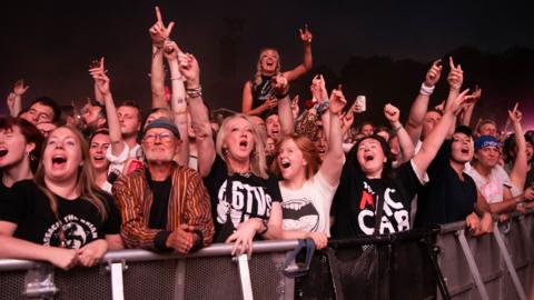 Front row of crowds at a concert, young and old scream and shout and look like they are having a great time