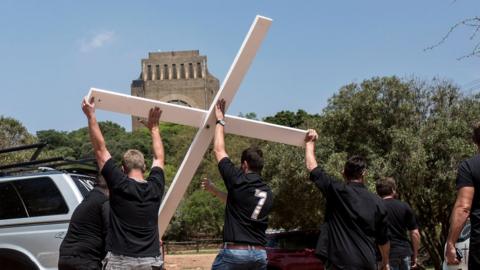 White South African activists haul a white cross aloft from the back of a jeep - to protest a rise in farm murders in the country.