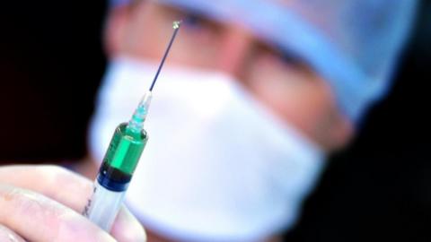 A doctor with a syringe. A drop of liquid is coming out of the needle.