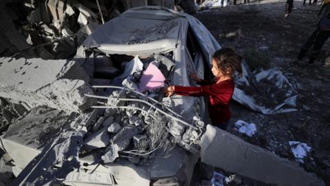 A Palestinian girl inspects a car destroyed by debris following an Israeli strike on a house in Jabalia, northern Gaza (14 May 2025)