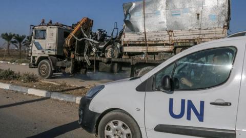 Destroyed truck used by Unrwa is loaded onto another truck with a UN-marked vehicle in the foreground