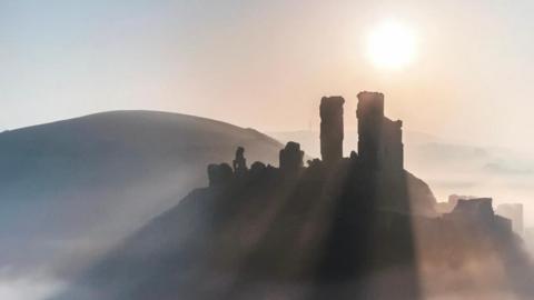 The ruins of Corfe Castle are silhouetted in mist and low sun