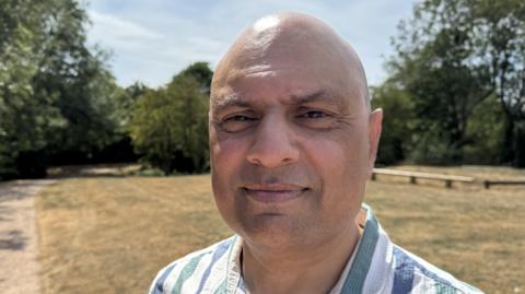 Harjit Singh Nijjer is smiling. He is standing in the park with trees behind him.