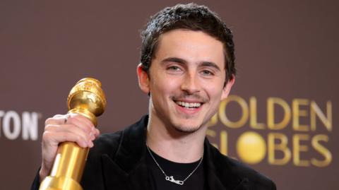 Timothée Chalamet holding up his Golden Globe and smiling