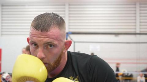 Leon Dunnett peeks out from behind yellow boxing gloves.