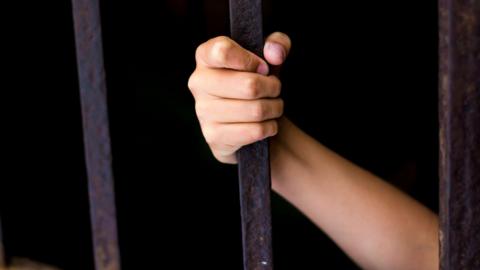 A child's hand gripping a jail bar