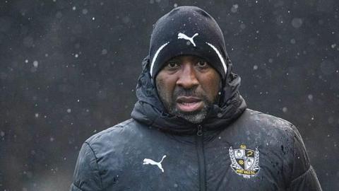 Darren Moore wearing his Port Vale beanie and puffer jacket looks straight ahead during a match