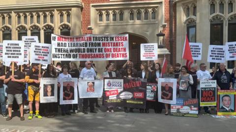 Bereaved families and friends stand in solidarity outside Arundel House in London where the Lampard Inquiry is taking place. They are all holding posters and placards of their loved ones or slogans representing why they want justice. One reads 'if mental health trusts in Essex had learned from mistakes there would only be one death instead of thousands of deaths'.