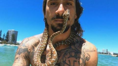 A man surfing with a snake around his neck