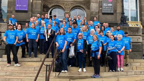 A group of people in blue t-shirts standing on a staircase with gold baton.