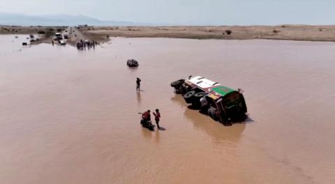 People stand next to an overturned vehicle in flood waters in Yemen. 