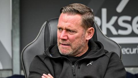A cross-looking Kevin Nolan, the Northampton Town manager, crosses his arms as he watches the action