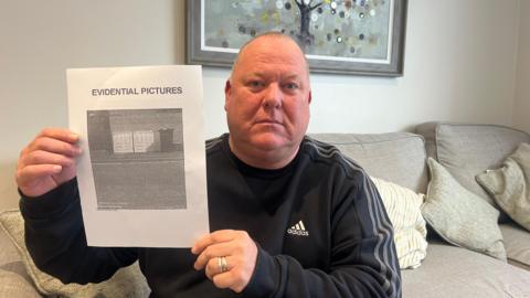 Damian Quillan sat on a sofa holding a piece of paper which says evidential pictures