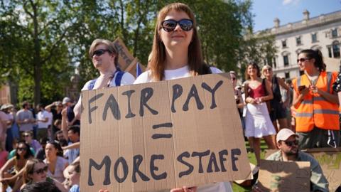 A woman holds a sign saying "fair pay equals more staff" during a junior doctors' strike