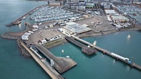 An aerial view of the Elizabeth Terminal at St Helier showing a large terminal building and a jetty and smaller craft moored in a harbour behind.