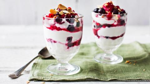 Two yoghurt parfaits are sitting on a green table cloth. 