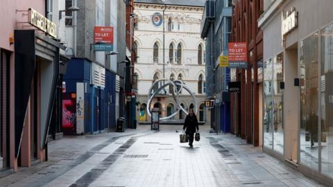 A woman walks along a deserted shopping street in Belfast city centre