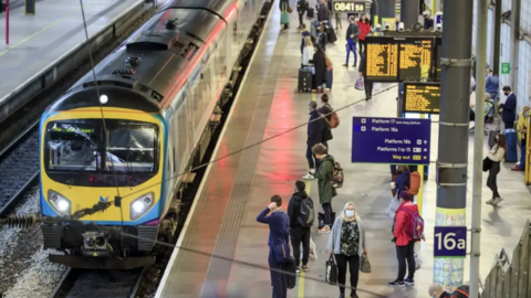 A station platform in Leeds, with a train waiting at the station. Passengers are waiting to board.