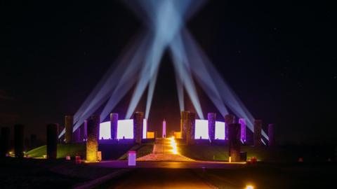 The National Memorial Arboretum illuminated in purple and warm yellow lights