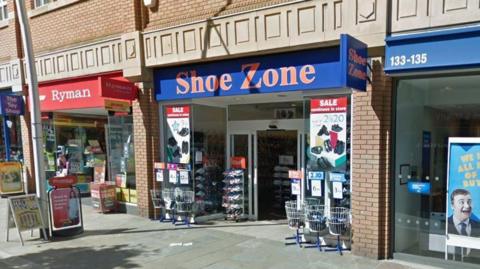 Street view image of former Shoezone next to a bank and Ryman shop on the other side.