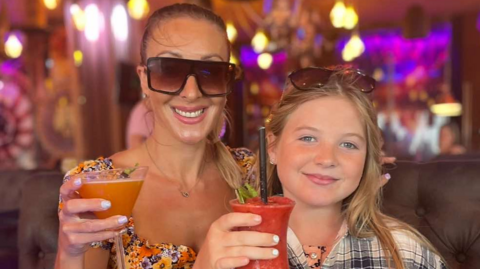 A picture of Gemma and Evie smiling into the camera holding drinks. 