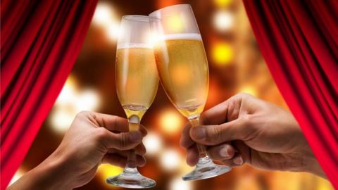 People clinking glasses of champagne in front of theatre curtains