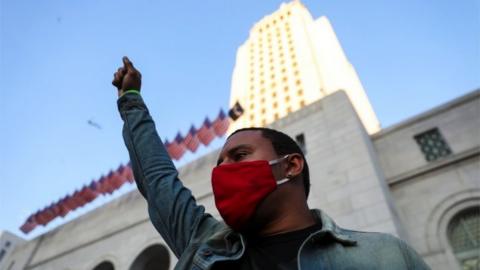 A man raises his fist as demonstrators gather in front of Los Angeles City Hall