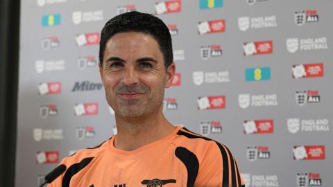 Mikel Arteta stifles a laugh while sitting at a press conference