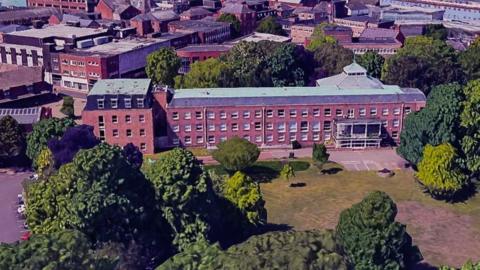 An aerial view of Wrexham Guildhall which is a large red building. In front of it is a lawn and trees