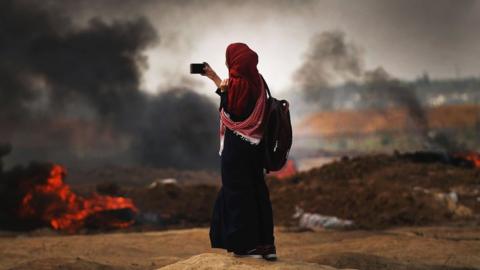 A Palestinian woman documents the situation at the border fence with Israel as mass demonstrations continue on May 14