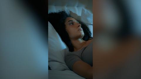 A woman with dark hair lies in bed