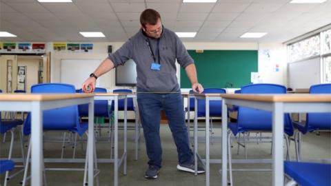 A school caretaker ensures desks are properly spaced