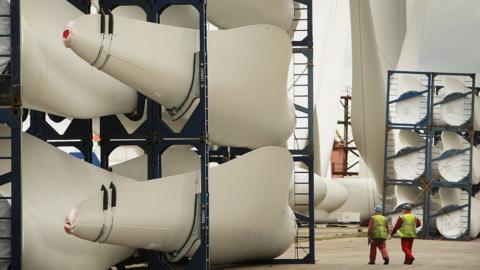 Workers pass stored wind turbine blades at the Harland & Wolff shipyard