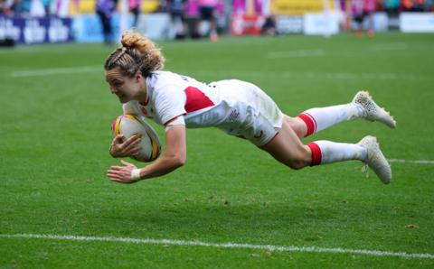 England rugby player Ellie Kildunne leaps through the air to score a try.
