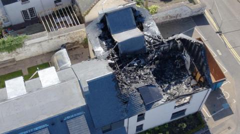 An aerial shot of a burned out building, where the roof has collapsed